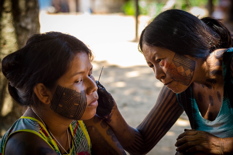 A Mebengokre mother paints the face of her daughter.