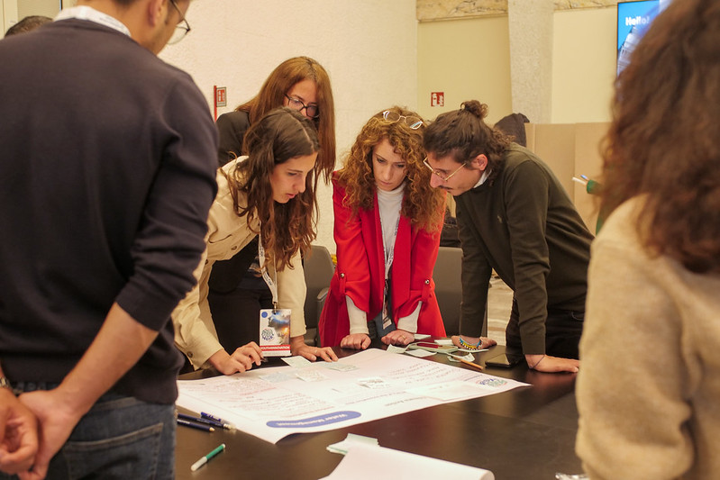 Four young people including a redheaded woman in a bright red jacket work on a design thinking exercise together.
