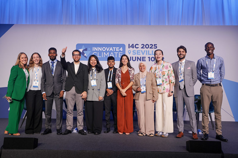 A diverse group of professionally dressed young people pose in front of a backdrop at Innovate4Climate in Sevilla.
