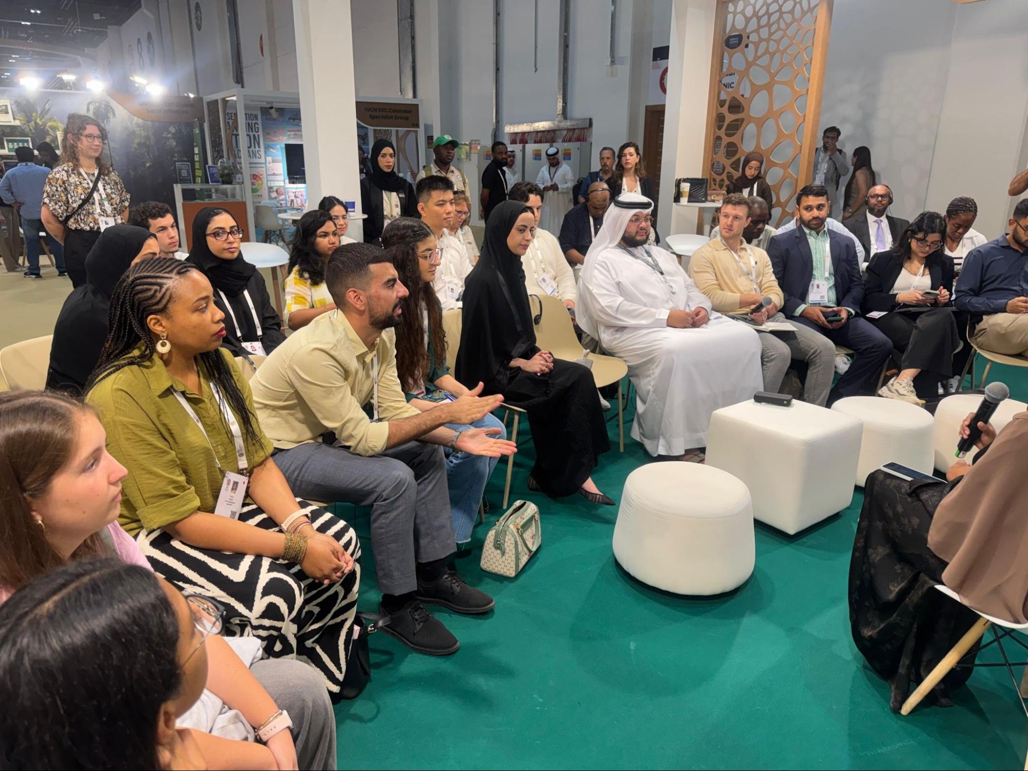 A number of young people in an arc of chairs have a moderated discussion.