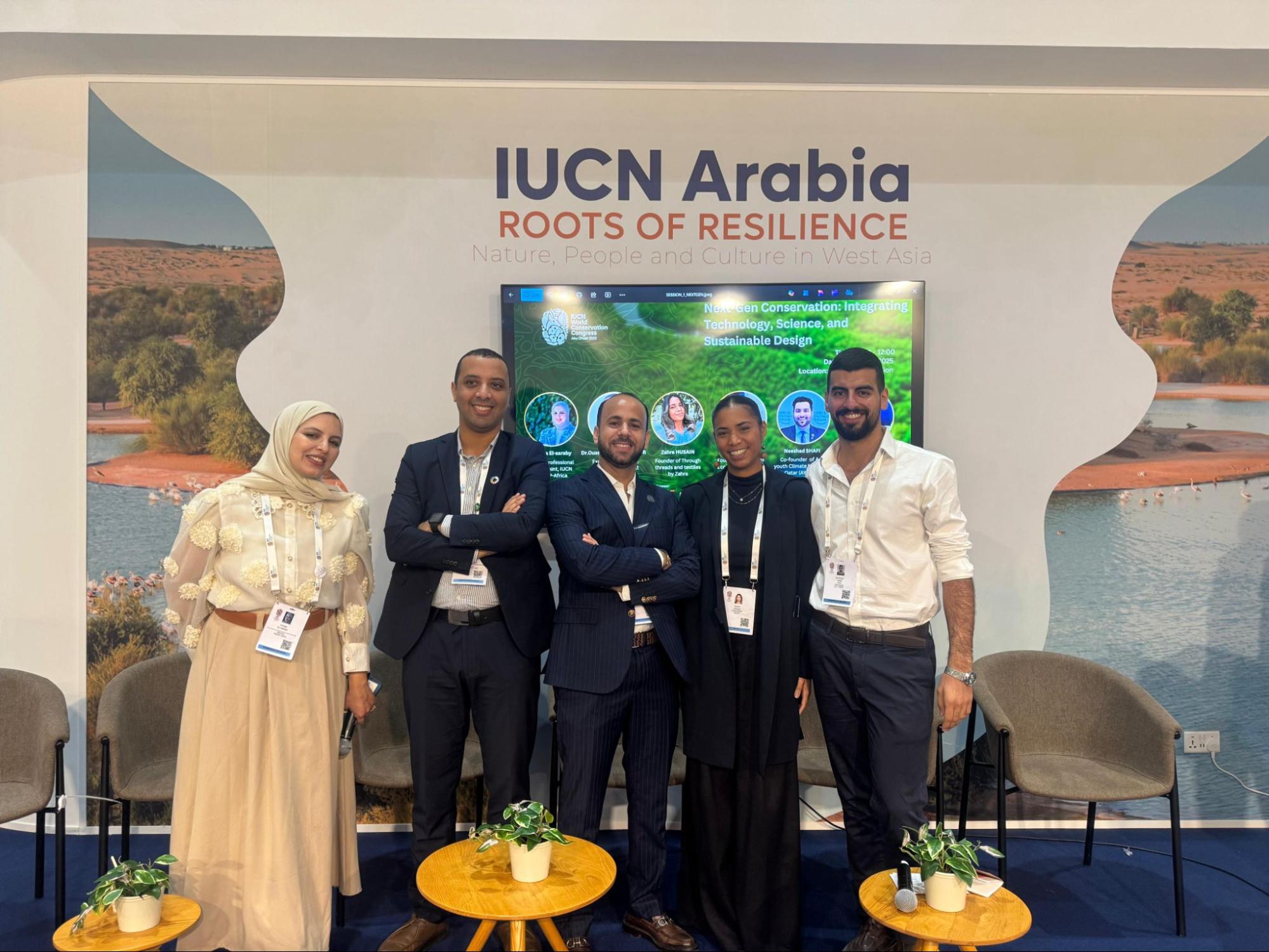 Five well-dressed young people smile for the camera below a sign reading "IUCN Arabia: Roots of Resilience."