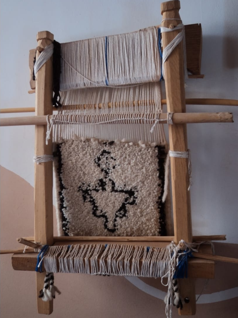 A rug bearing a traditional Amazigh fibula symbol in progress on a loom.