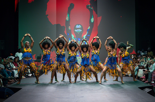 African dancers in gold and blue dance in sync for a crowd.