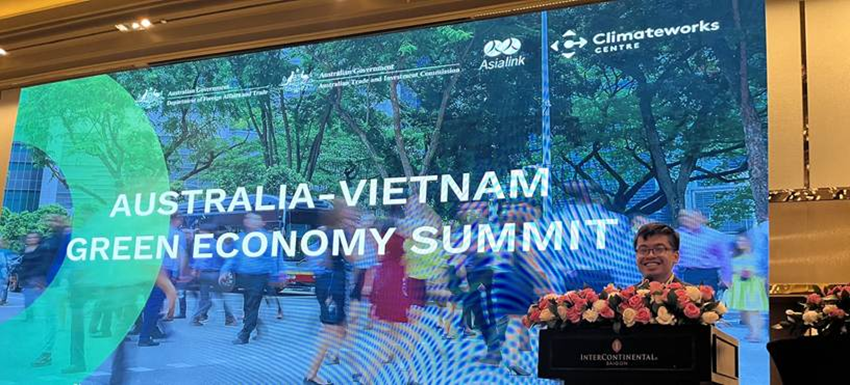 A smiling young man approaches a lectern. The large banner behind him reads "Australia-Vietnam Green Economy Summit."