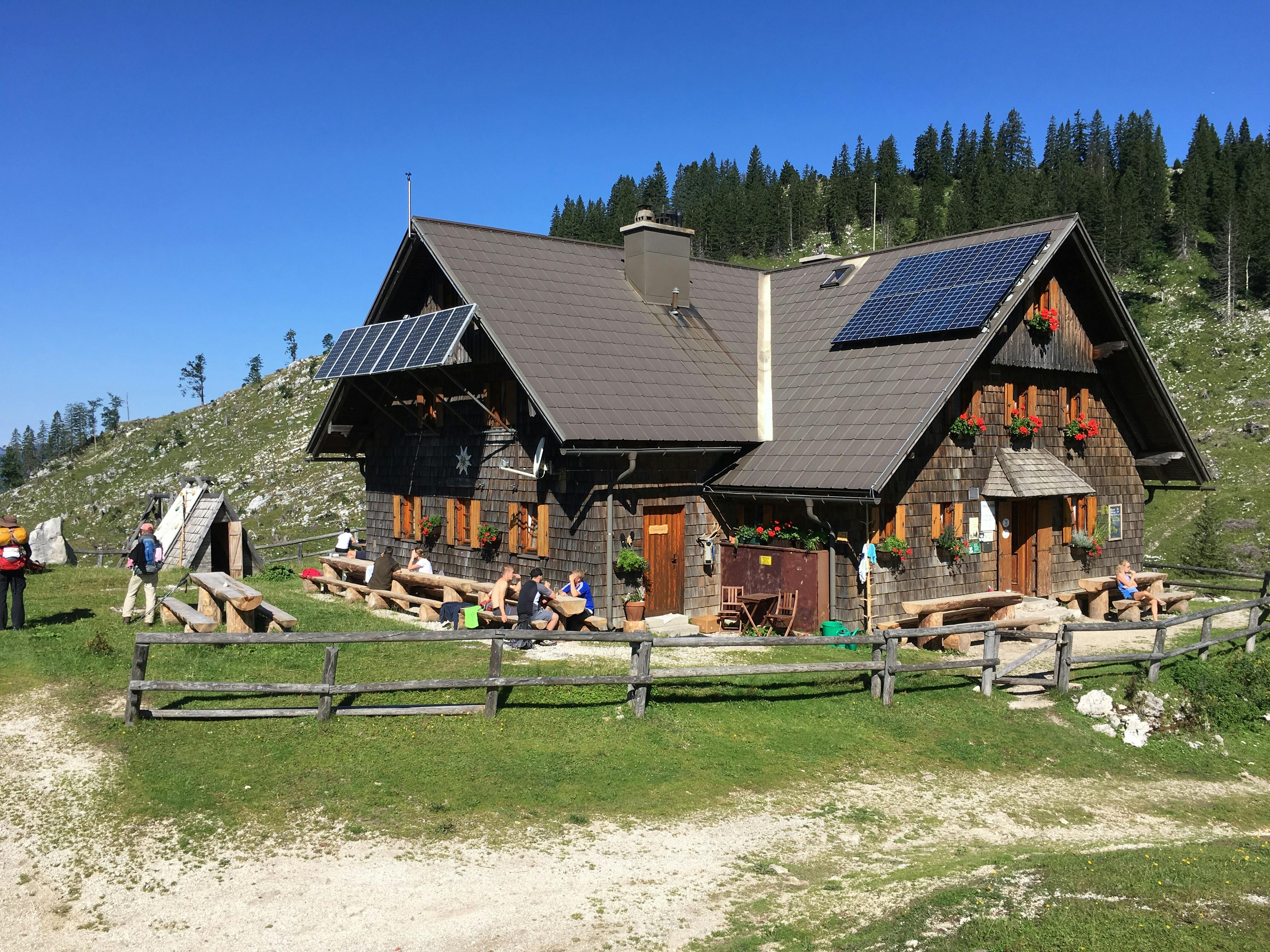 A mountain lodge with solar panels. Backpackers sit on benches outside.